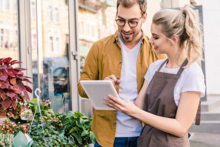 smiling florist and customer using tablet together at flower shop