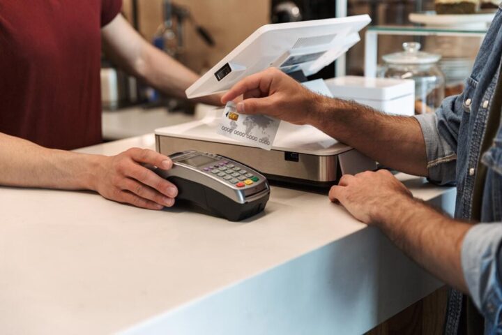 Cropped photo of caucasian man paying debit card in cafe while w